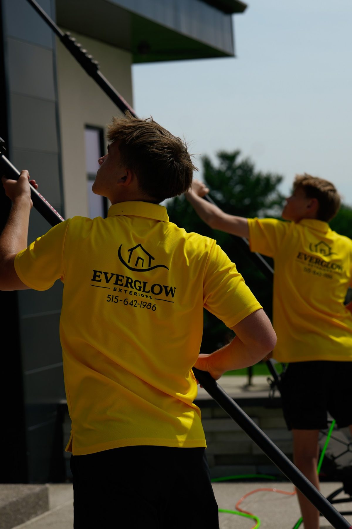 Two EverGlow Exteriors crew members in yellow polos cleaning windows with water-fed poles